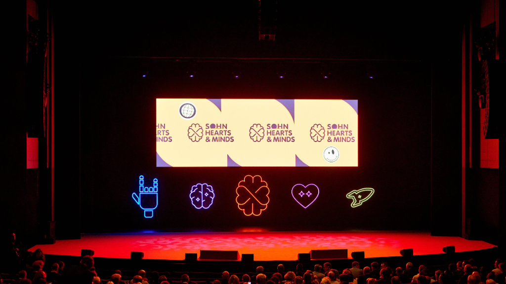 A hanging LED screen displaying an organisation's logo. Underneath there are five custom designed LED lights in the shape of a heart, rocket ship, brain, the 'rock and roll' hand sign and the organisation's logo each in different colours.