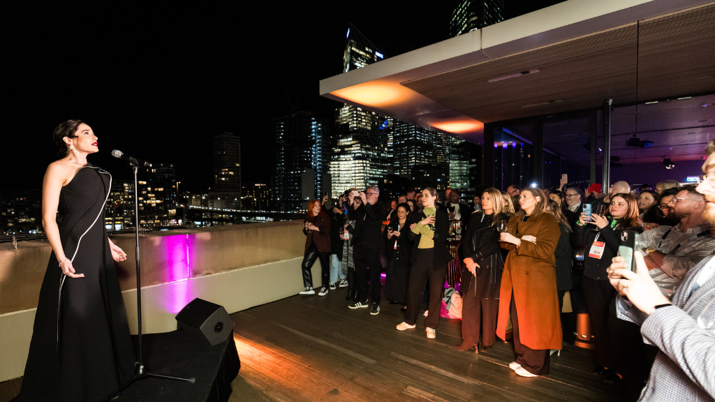 A musical artist performing on stage outdoors on the MCA Harbourside Room terrace overlooking Circular Quay. 