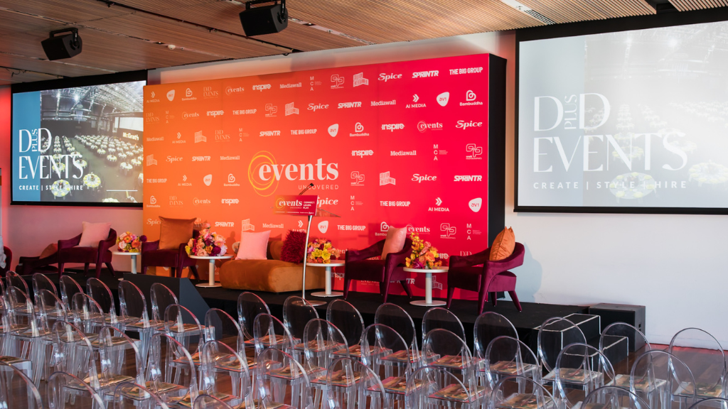 Chairs set up on stage in a panel style format between two projection screens displaying content for the event.